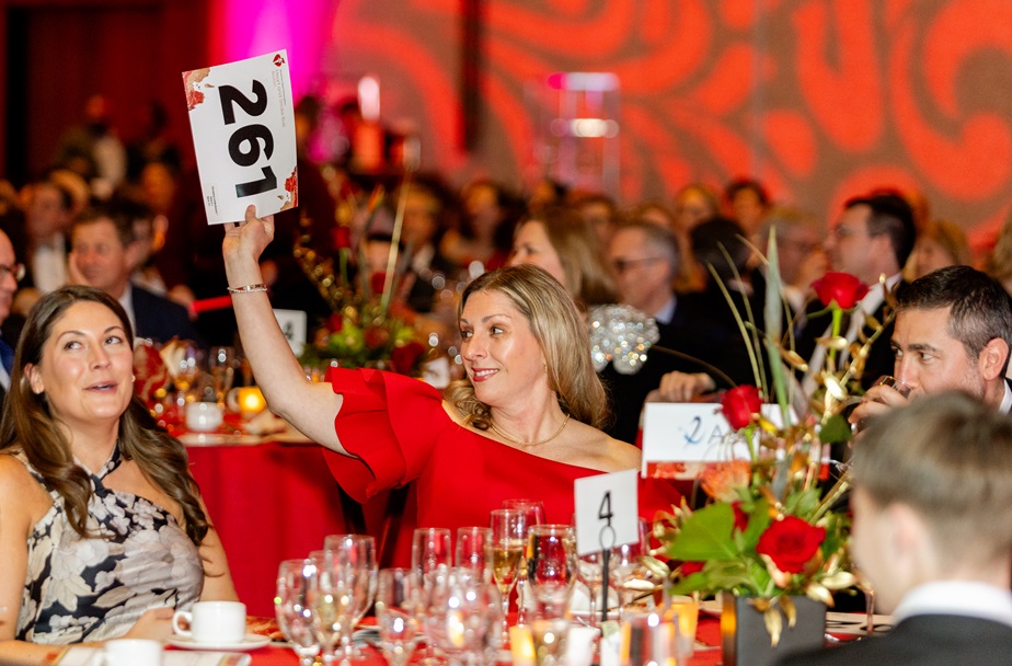 Woman seated in a crowded ballroom holding up bidder number 261.